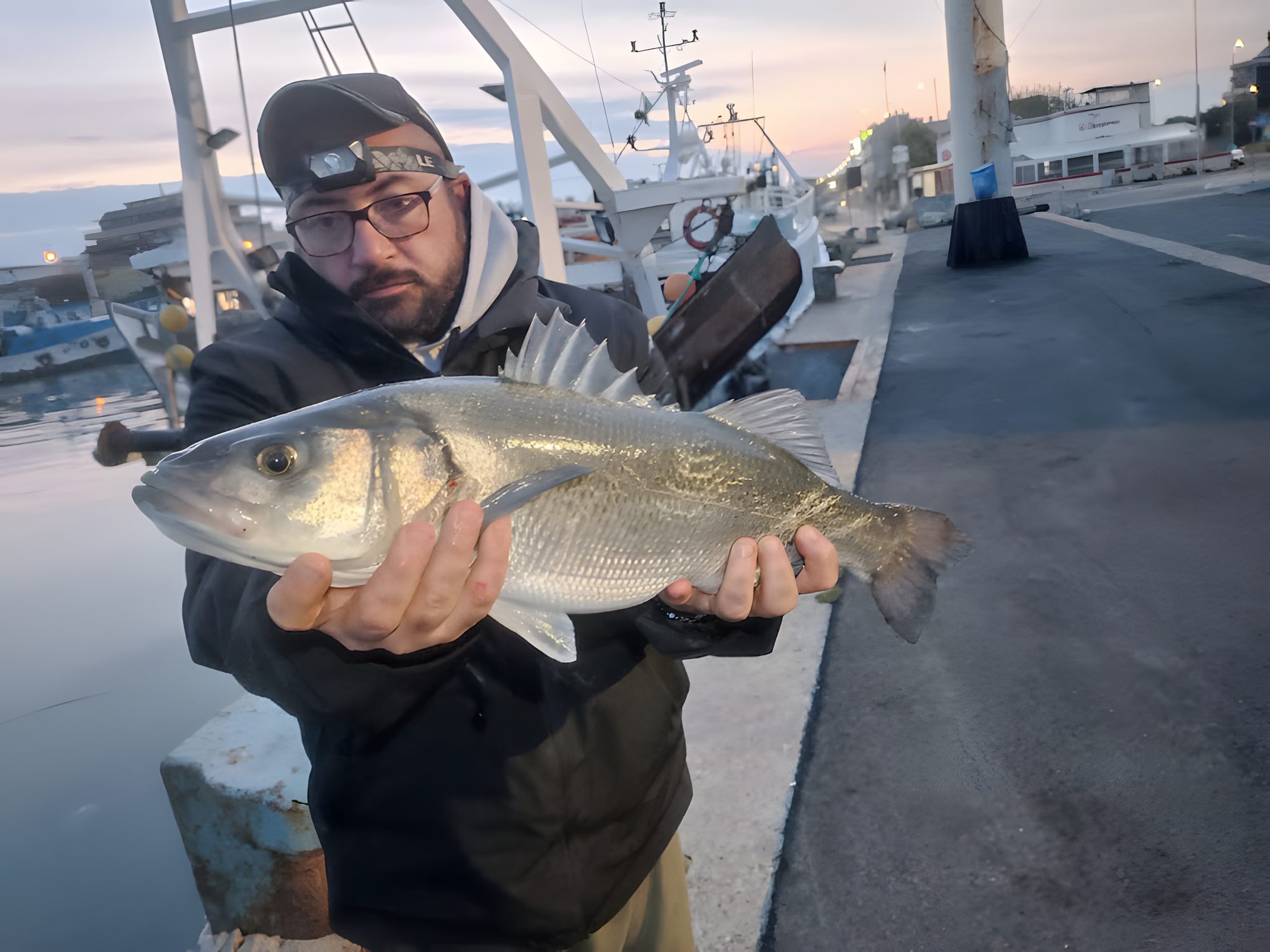 Enrico Avagliano con una spigola in mano al porto, all'alba